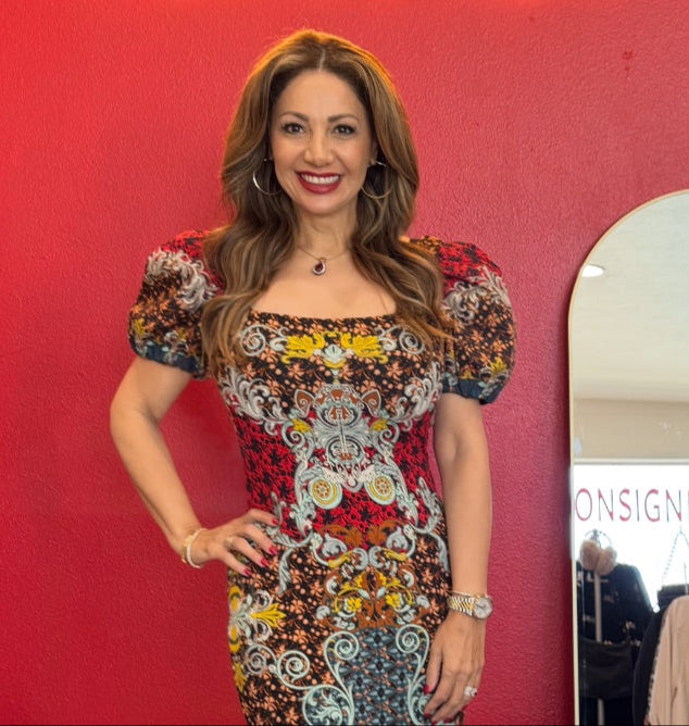 Woman in a patterned dress standing in front of a red wall with 'Savvy Girls Do Resale' neon sign.
