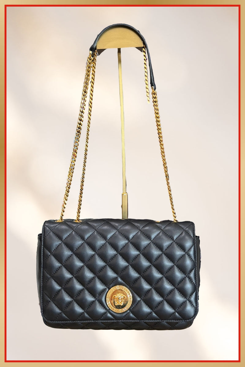 Black quilted handbag with gold chain strap and emblem on a light background