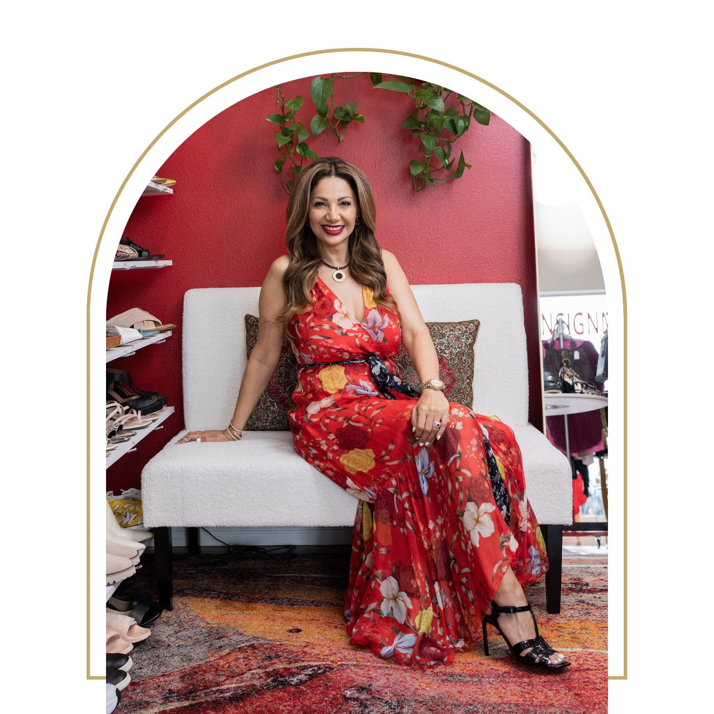 Woman in a red floral dress sitting on a white chair against a red wall.